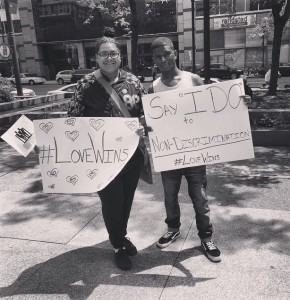 Two young people holding up signs reading "#LoveWins" and "Say 'I DO' to Non-Discrimination"